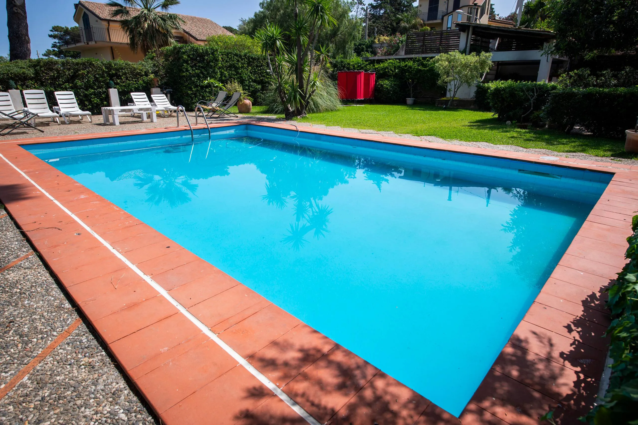 Piscina con solarium, lettini e doccia esterna nel parco della villa