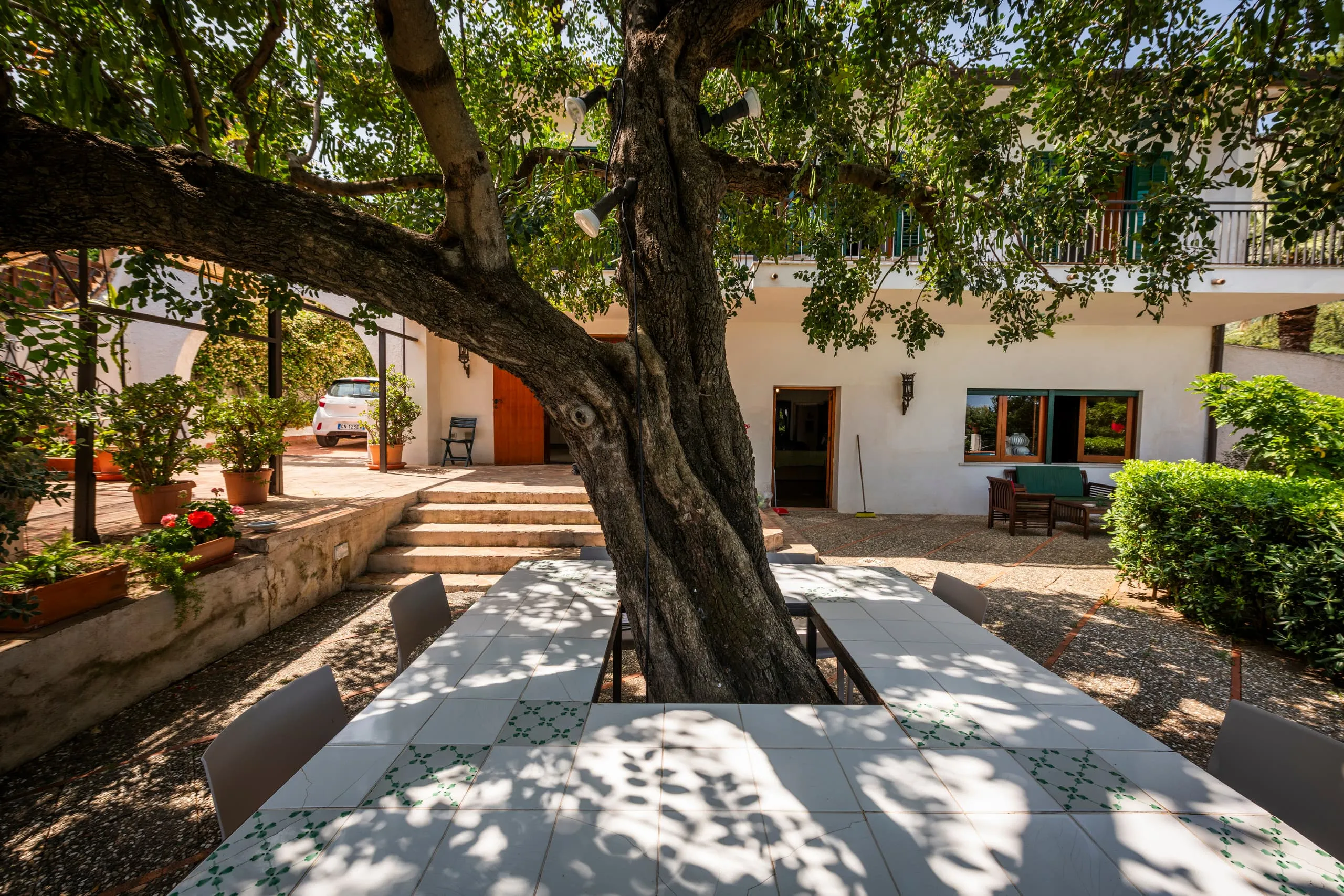 Facciata della villa con tavolo all’ombra del grande carrubo