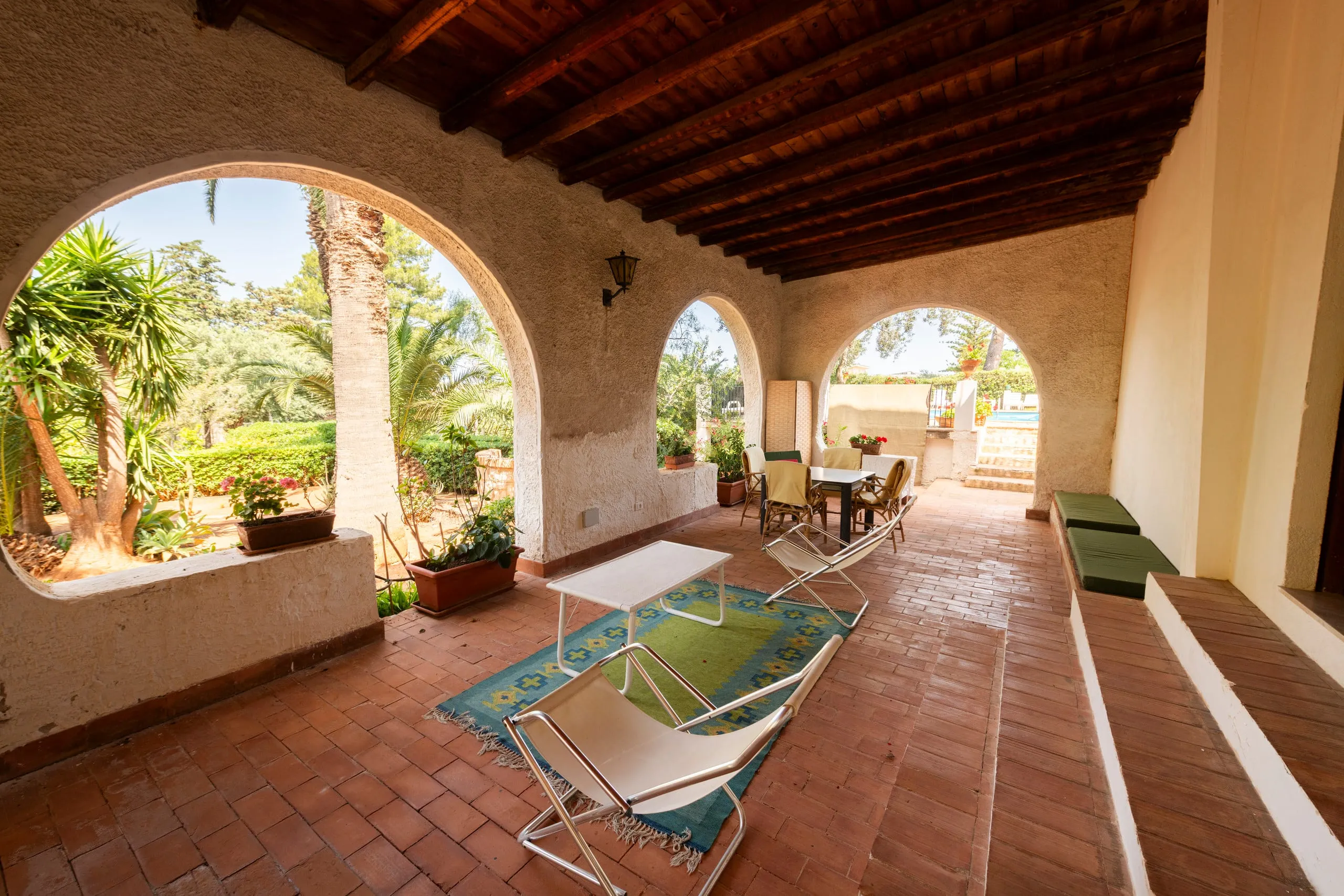 Loggia ad archi con poltrone e tavolo affacciata sul giardino di palme