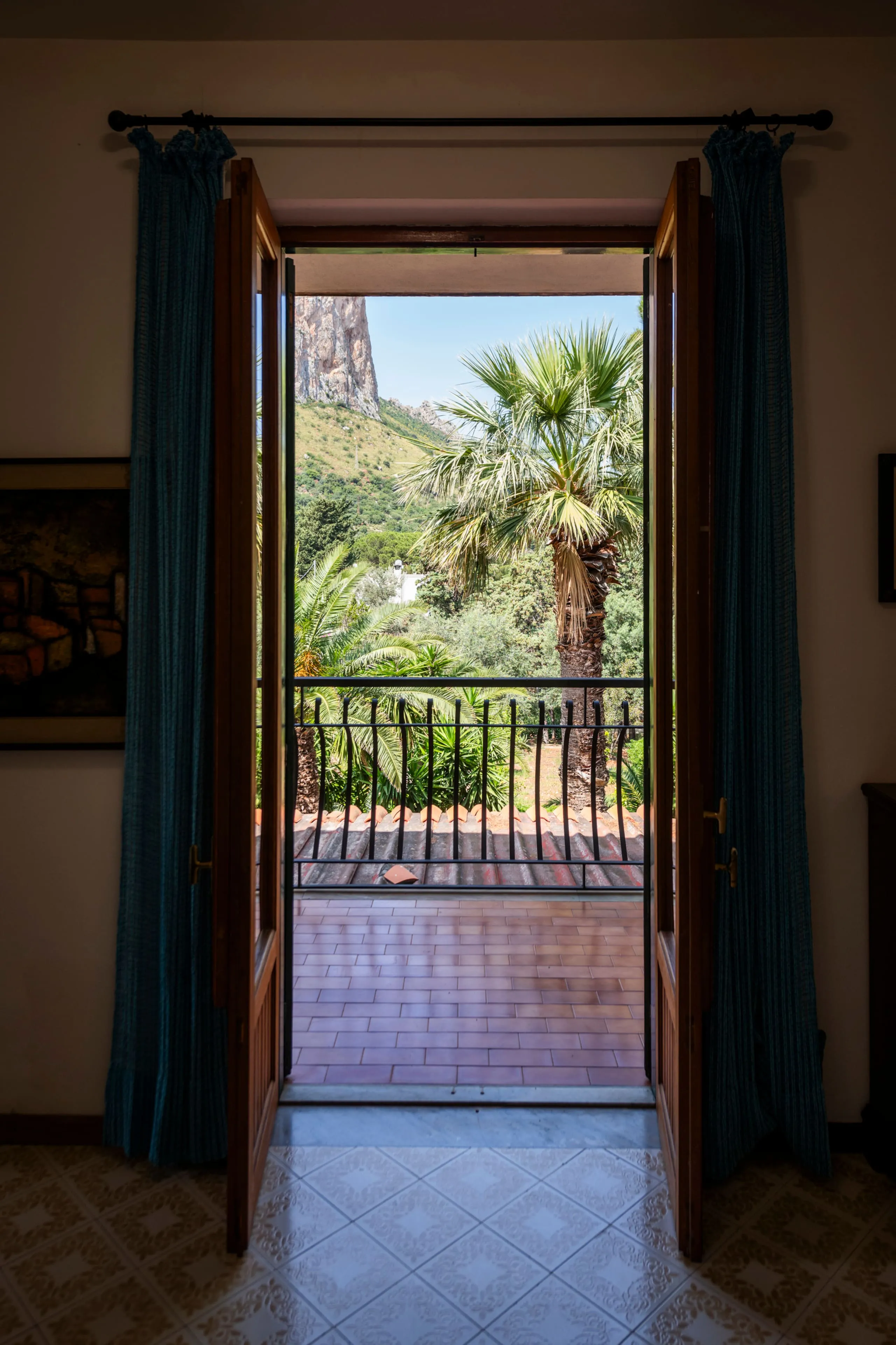 Porta-finestra aperta sul balcone con vista su palme e montagna